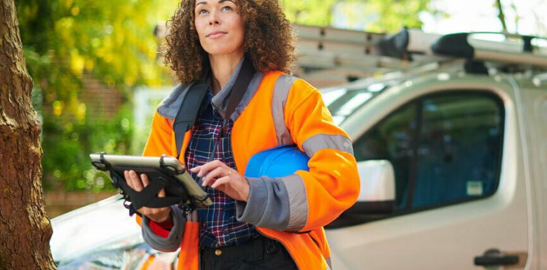 Female tradesperson reviewing job details on a tablet beside a work van